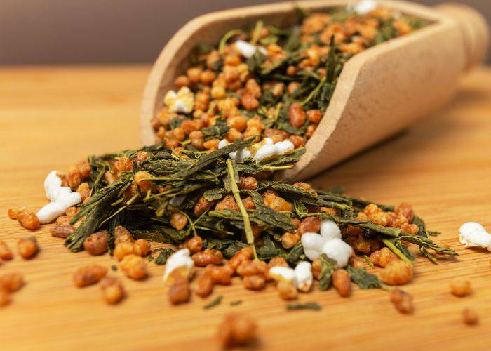 A wooden scoop overflowing with the tea leaves and brown rice of Japanese genmaicha.